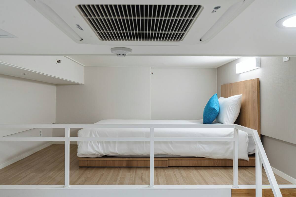 A compact, modern room with a bunk bed, white walls, and a wooden floor.