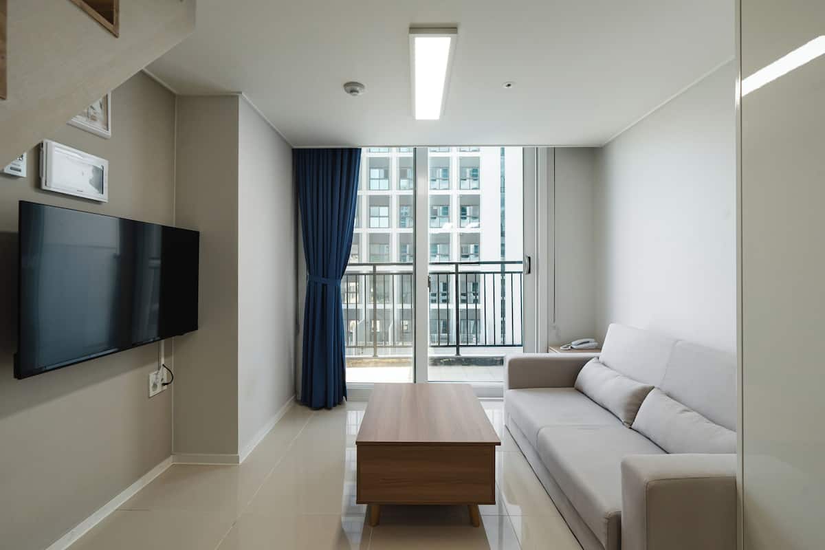 A modern living room with a flat-screen TV, a wooden coffee table, a sofa, and a balcony with a railing.