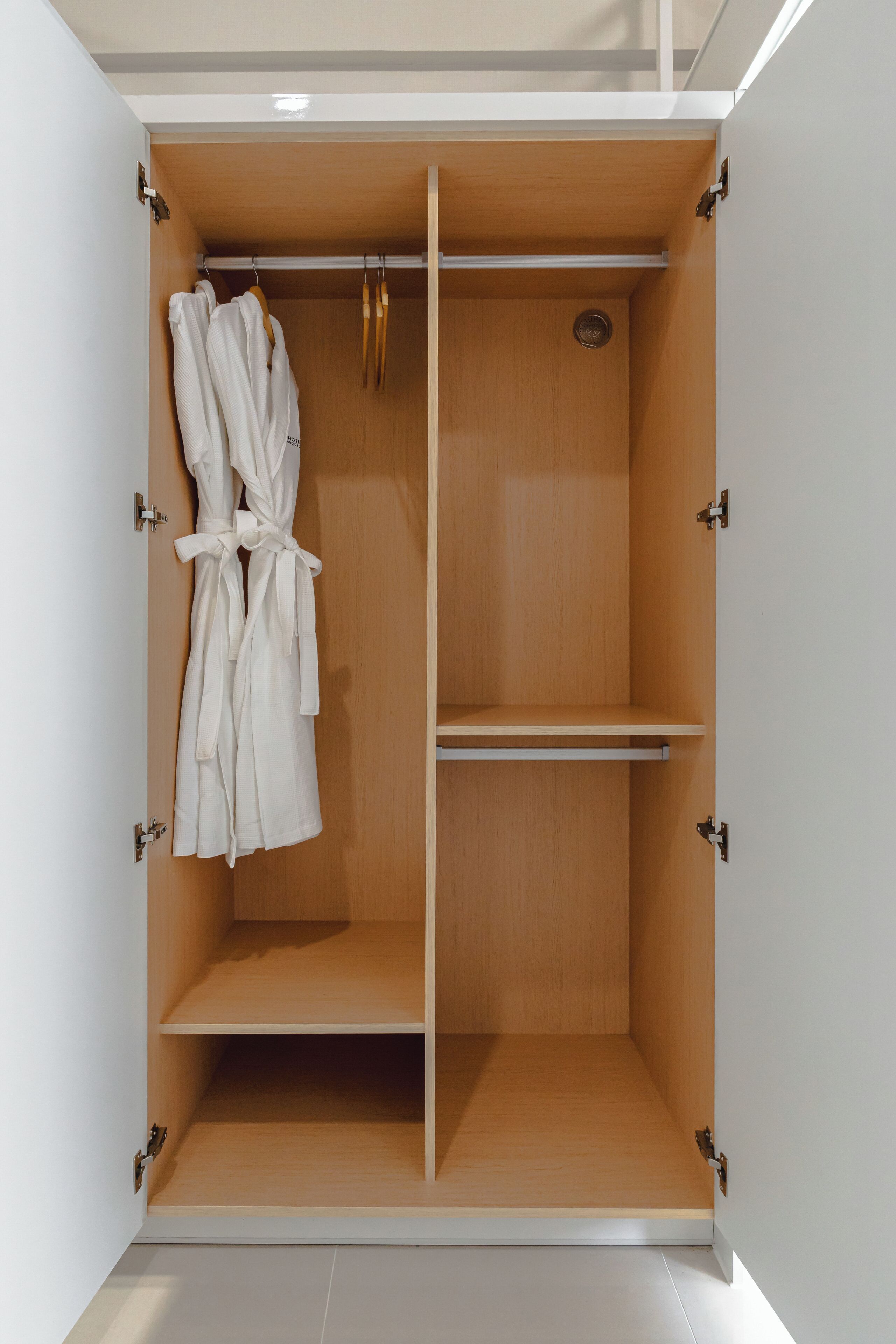 A walk-in closet with wooden doors, a robe hanging on the left, and a shelf unit in the center.