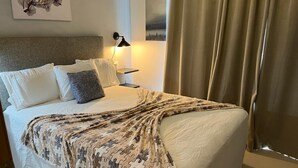 Una cama bien hecha con una colcha estampada, una lámpara de noche y un cuadro en la pared.