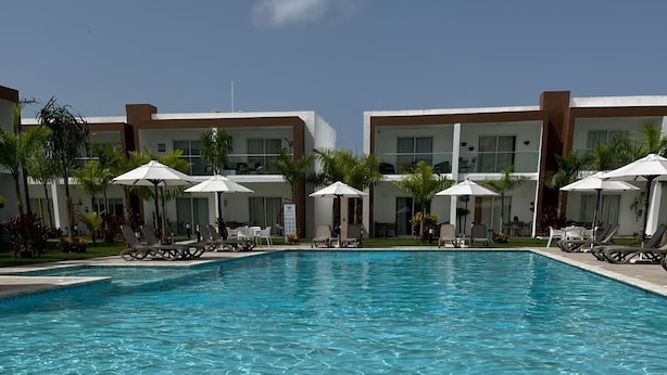 Una piscina cristalina con sillas de descanso y sombrillas, rodeada de edificios modernos.