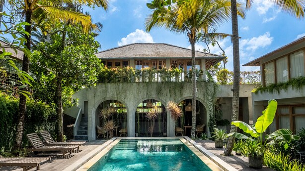 A swimming pool with clear water, surrounded by palm trees and a building with arches. - Ubud Terrace by Betterplace (Ubud)