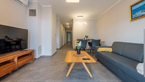 A modern living room with a flat-screen TV, wooden entertainment unit, grey sofa, and a dining area with a wooden table and chairs.
