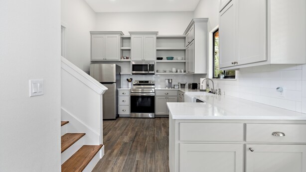 A modern kitchen with white cabinetry, stainless steel appliances, and a wooden staircase. - Edge of Main 5- Vineyard Views! (Fredericksburg)
