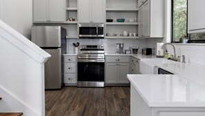 A modern kitchen with white cabinetry, stainless steel appliances, and a wooden floor. - Edge of Main 5- Vineyard Views! (Fredericksburg)