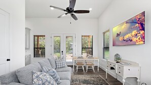 A modern living room with a gray sofa, a dining table with chairs, a white sideboard, and a ceiling fan. - Edge of Main 5- Vineyard Views! (Fredericksburg)
