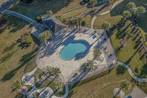 An aerial view of a property with a swimming pool, paved walkways, and landscaped areas with palm trees.