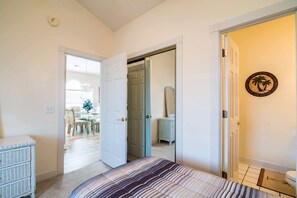 A bedroom with a bed, a dresser, a door leading to another room, and a wall-mounted mirror.