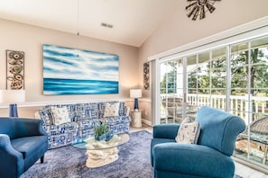 A living room with a large window, a sofa, two armchairs, a coffee table, and a painting of a seascape.