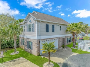 A two-story house with a garage, surrounded by a well-maintained lawn and palm trees.