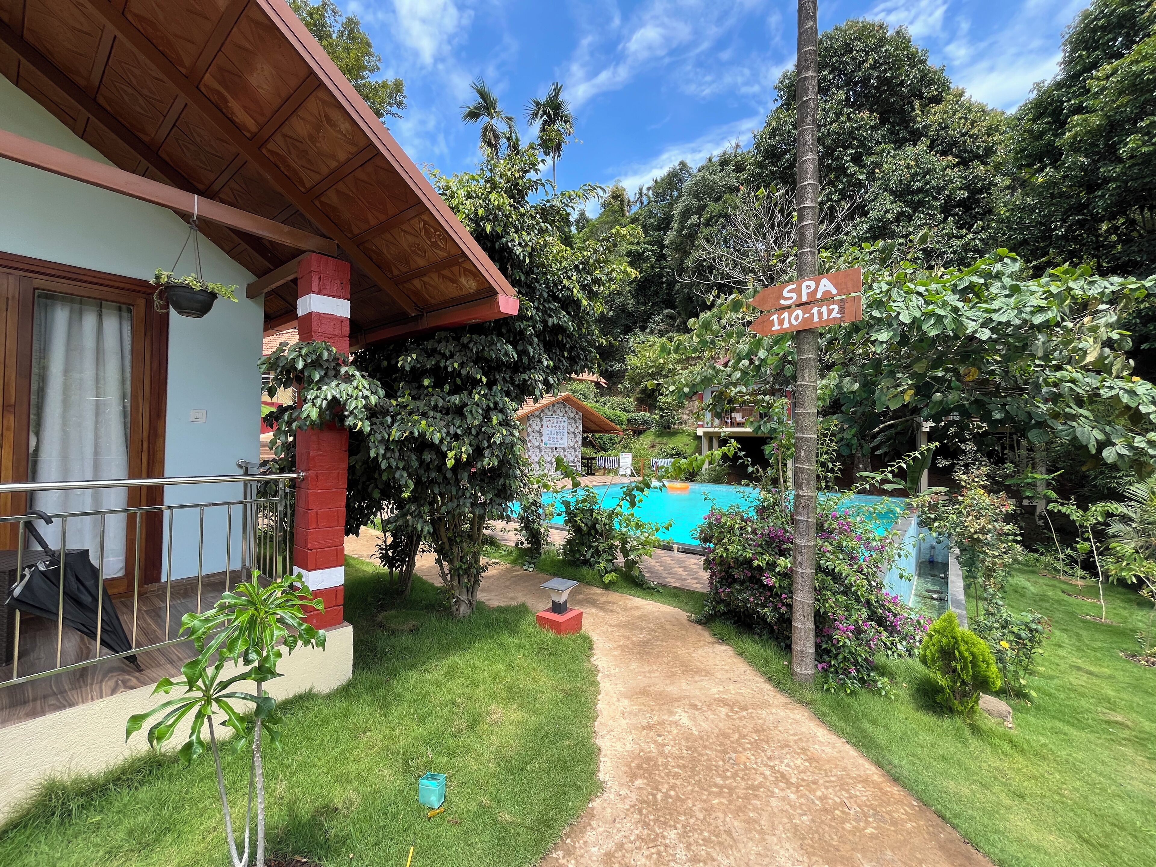 A spa area with a pool, surrounded by lush greenery and a wooden building with a red and white facade.