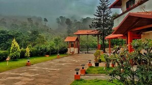 A pathway leading to a building with a red roof and a small structure with a red roof. - Hill Crest Resort (Madikeri)