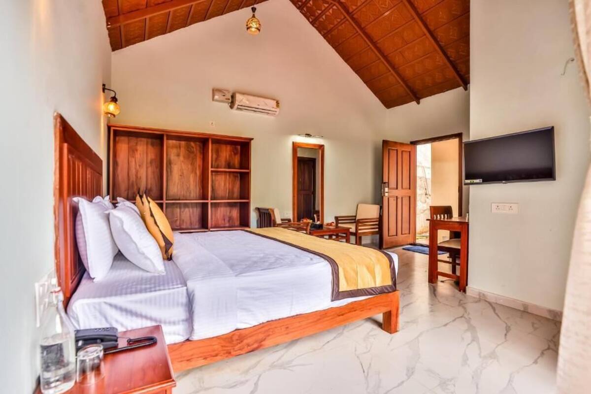 A spacious bedroom with a large bed, wooden headboard, a TV mounted on the wall, and a wooden wardrobe.