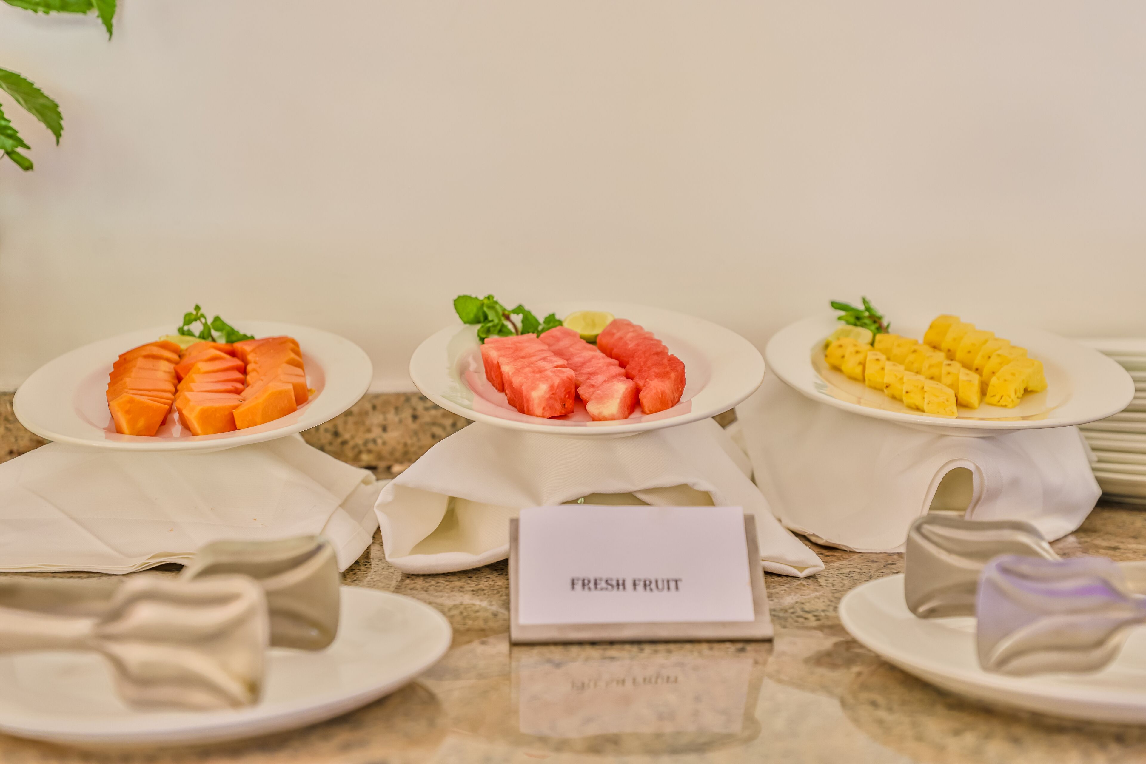 A breakfast buffet with plates of fresh fruit, including orange slices, watermelon, and corn.