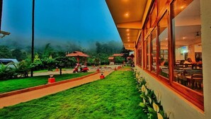 A restaurant with outdoor seating, a pathway, and a view of the surrounding greenery. - Hill Crest Resort (Madikeri)