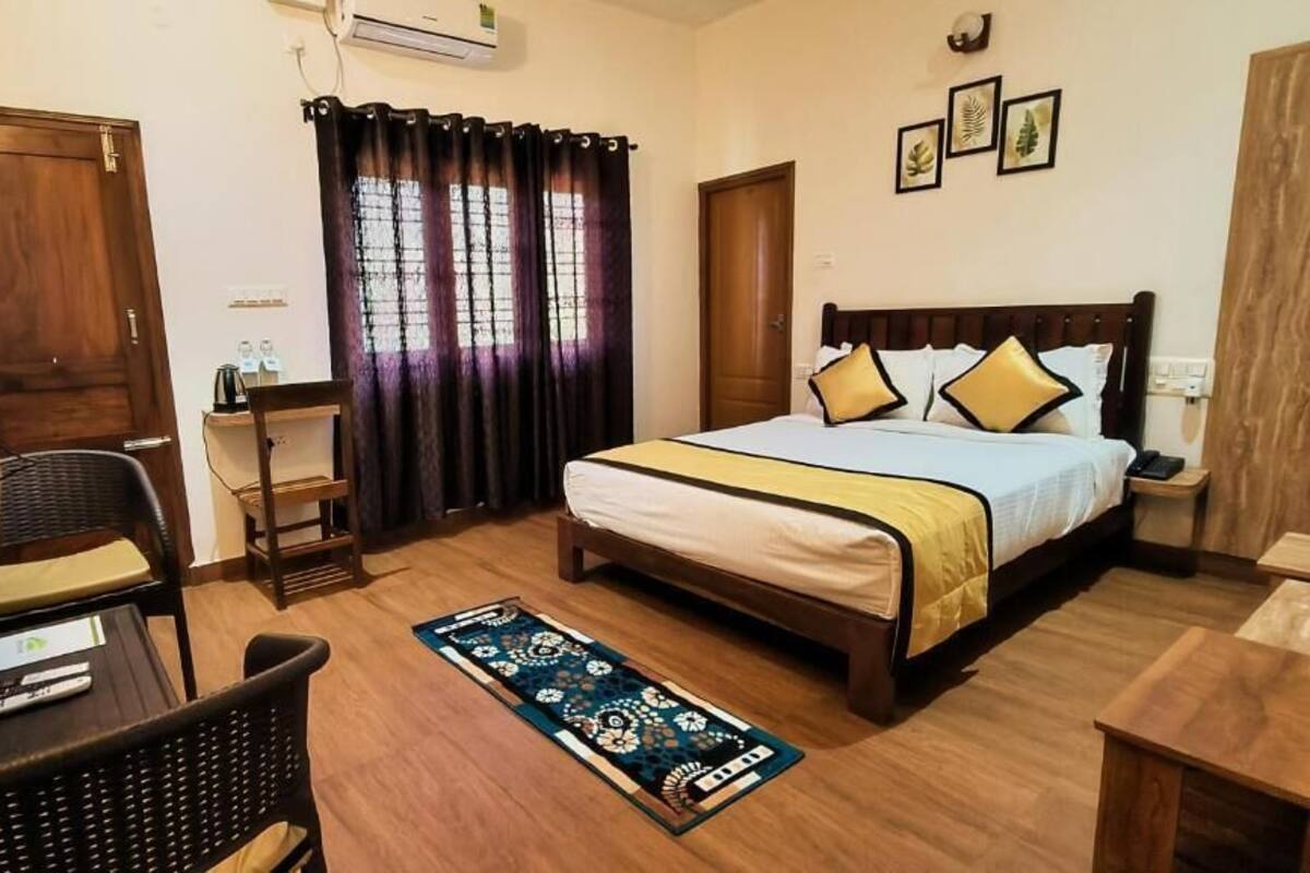 A bedroom with a bed, a desk, a chair, a TV, and a window with curtains.