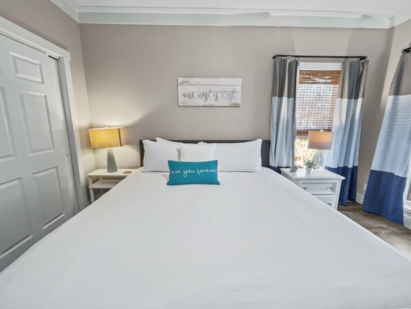 A neatly arranged hotel room with a large bed, a bedside table with a lamp, a wall-mounted sign, and a window with curtains. - "Pinewood" | Inlet Beach | Dog Friendly | Grill and Firepit (Inlet Beach)