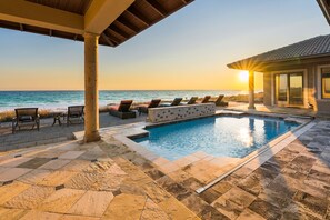 A pool area with lounge chairs and a view of the ocean at sunset.