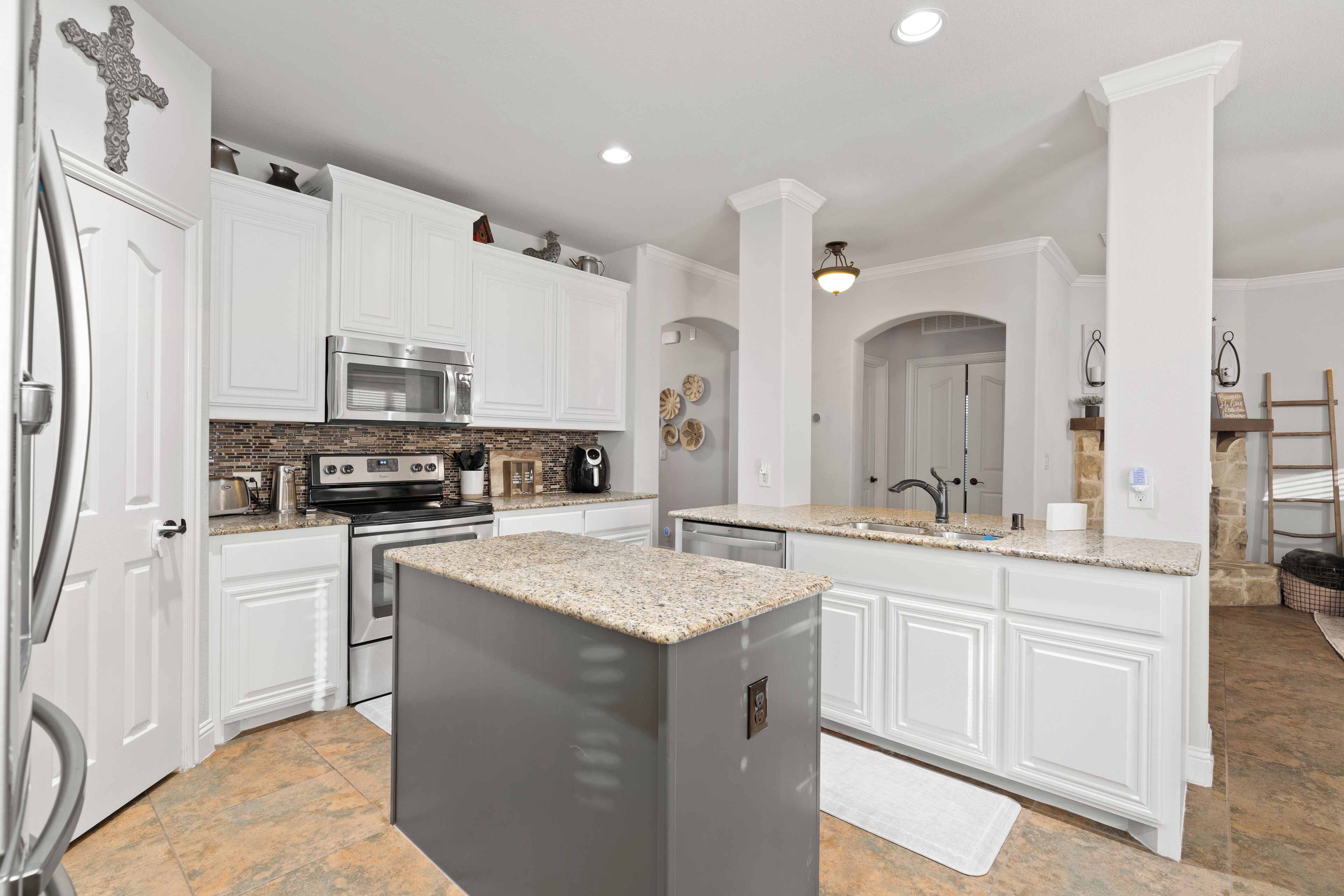 A kitchen with white cabinets, a granite countertop, stainless steel appliances, and a cross decoration on the wall.