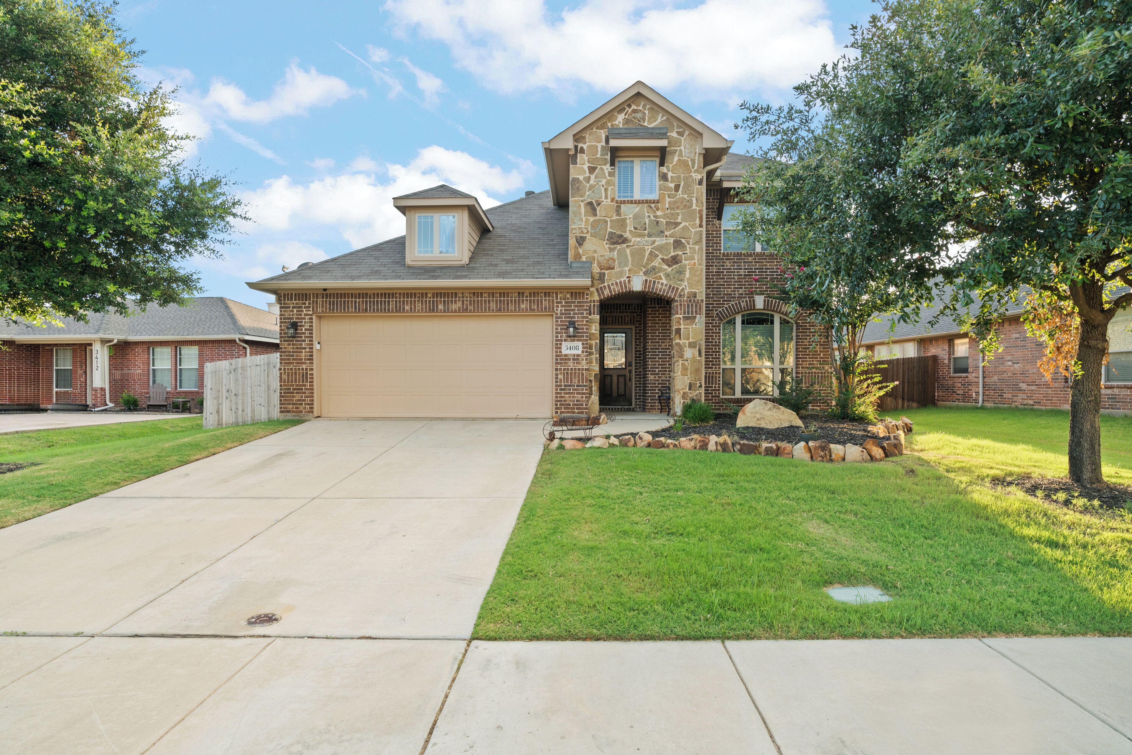 A two-story house with a stone facade, a garage, and a well-maintained lawn.
