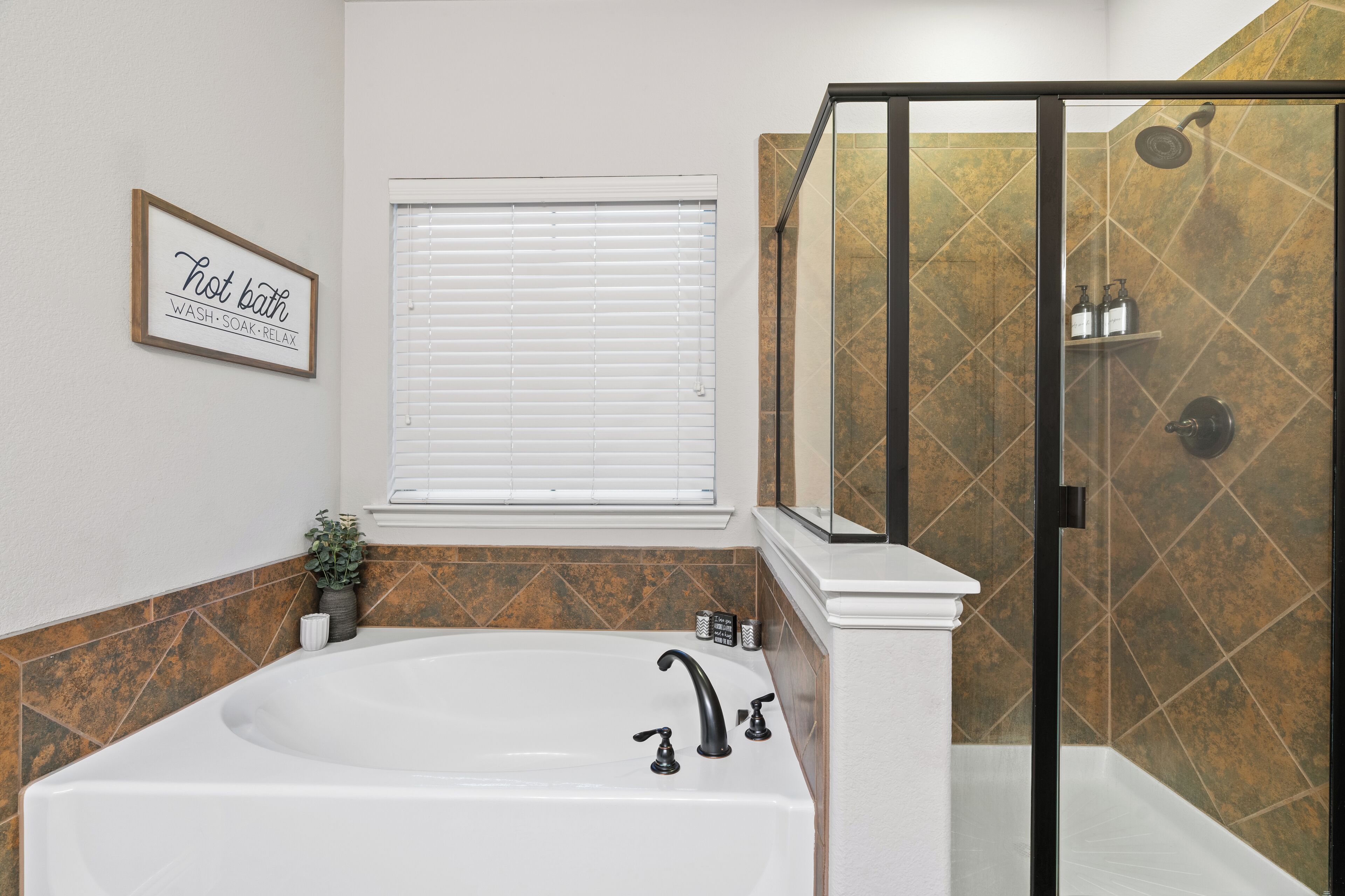 A bathroom with a large bathtub, a shower enclosure, and a window with blinds.