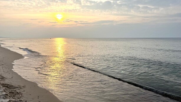 A beach with a calm sea and a sunset.