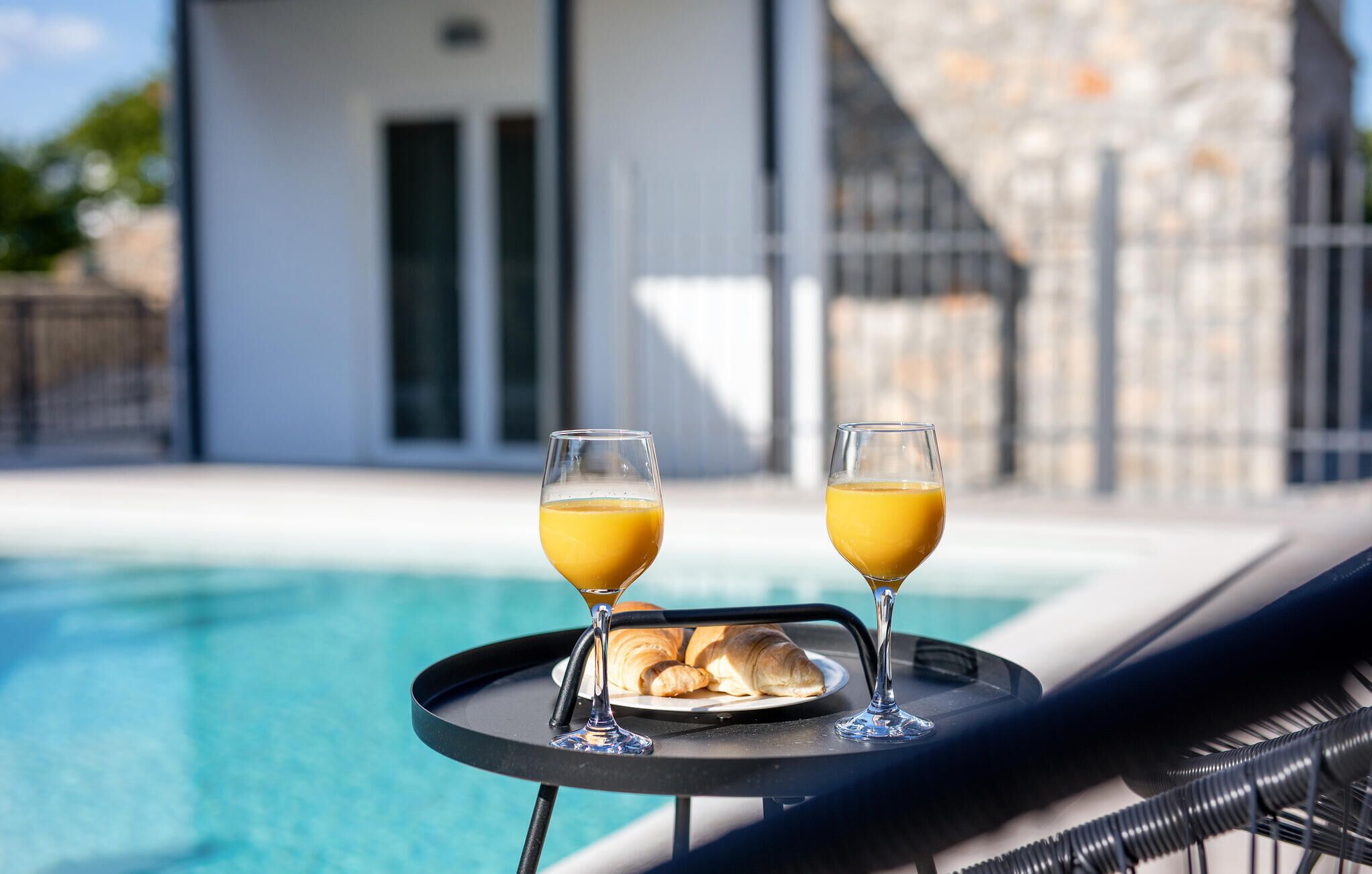 Uma bandeja com dois copos de sumo de laranja e croissants junto a uma piscina.