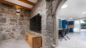 A stone wall with a wooden bench and a TV mounted on it. There is a dining area with chairs and a table. - Gorgeous home in Lakmartin (Lakmartin)