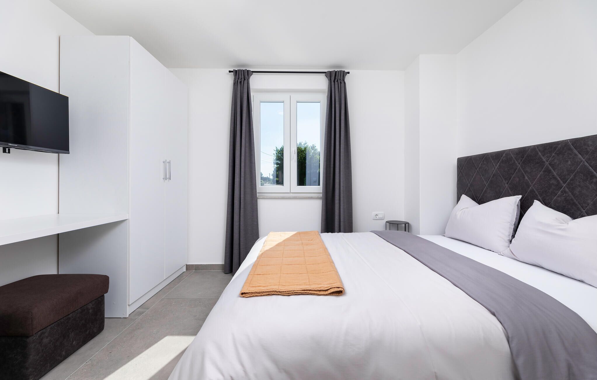 Una habitación de hotel moderna con cama, televisor, armario y ventana con cortinas.