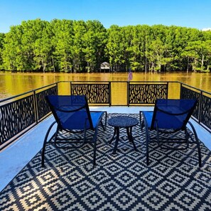 Un pont de bateau avec deux chaises et une petite table, entouré d’un sol à motifs et d’une rambarde.