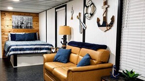 A room with a bed, a leather sofa, a wooden cabinet, and nautical-themed decor.