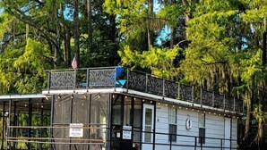 A houseboat with a covered deck, windows, and a flag.