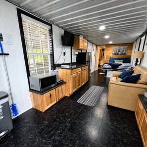 Een ruimtelijk ingerichte woonruimte met kitchenette, een slaapbank, een bed en een televisie.