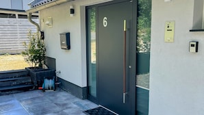 A modern building with a tiled roof, a numbered door, and a small outdoor area with steps and a planter. - Ruhiges Apartment am Waldrand (Geisenheim)
