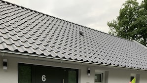 A modern building with a tiled roof, a black door with the number 6, and a small window. - Ruhiges Apartment am Waldrand (Geisenheim)