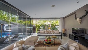 A modern living room with a glass wall overlooking a pool, a sofa set, a TV, and a bull skull decoration.