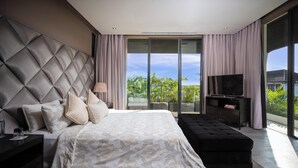A modern bedroom with a large bed, a TV, and a balcony with a view of greenery.