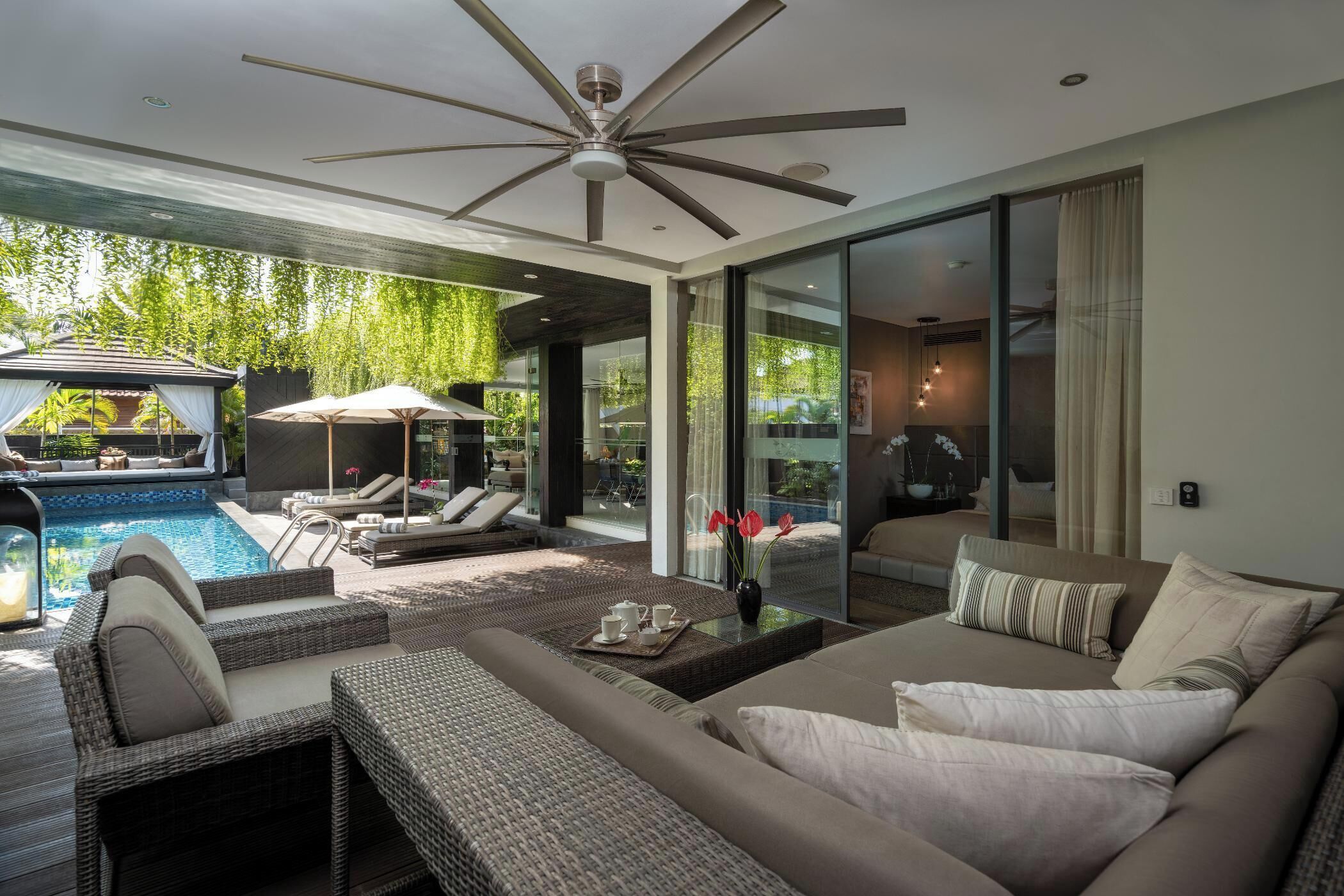 A modern living area with a ceiling fan, a pool, and a glass door leading to a balcony.