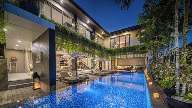 A modern hotel with a large indoor swimming pool, outdoor seating, and lush greenery.