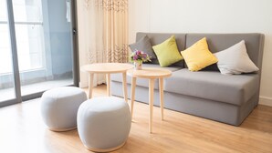 A modern living room with a grey sofa, two round ottomans, and a small table with a vase of flowers.