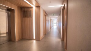 A modern hotel corridor with wooden paneling, recessed lighting, and a tiled floor.