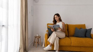 A person sitting on a mustard-colored sofa reading a book, with a small wooden stool and a white mug on the floor. - The Sorolla Apartment V | AC & WiFi | 4 Guests (Valencia)