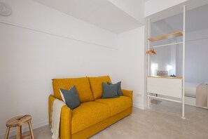 Um quarto com um sofá amarelo mostarda, um banquinho de madeira e um guarda-roupa branco com espelho.
