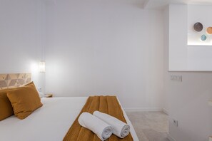 A hotel room with a bed, two pillows, a rolled towel, a wall-mounted light, and a wall with three circular decorations.