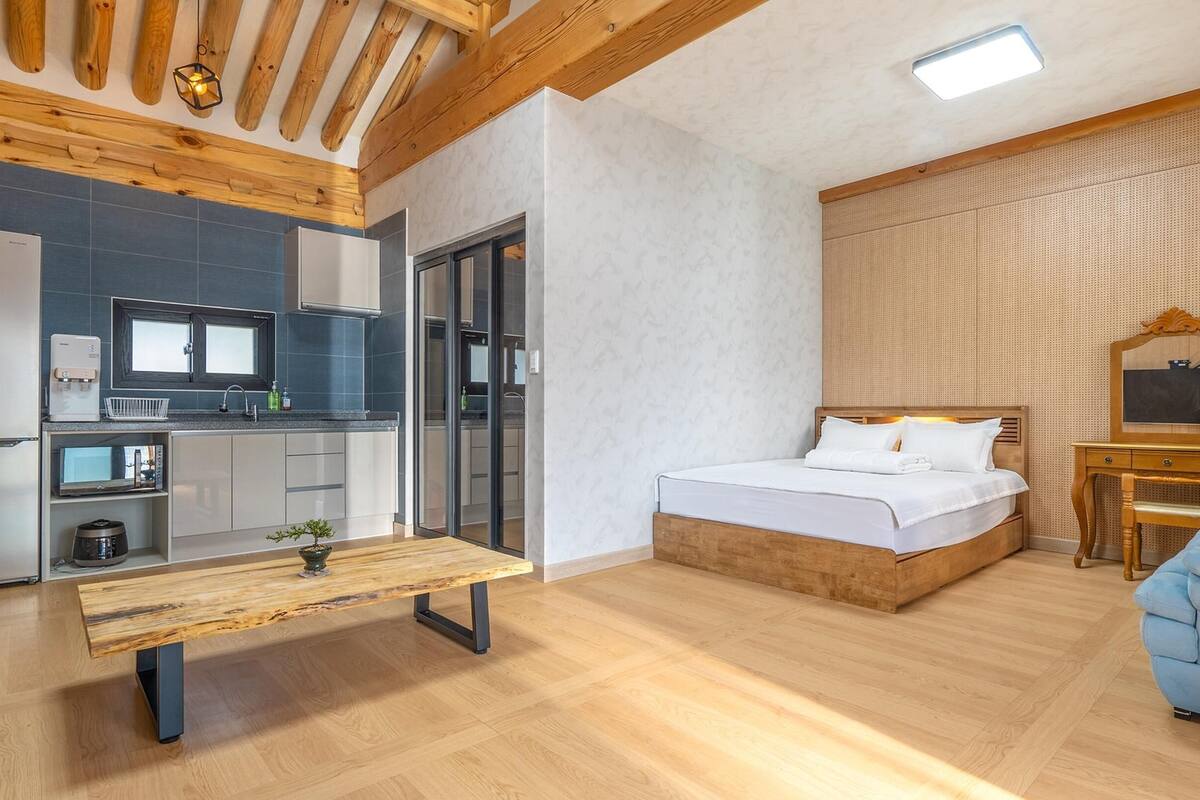A modern hotel room with a wooden bench, a bed, a desk, and a kitchenette.