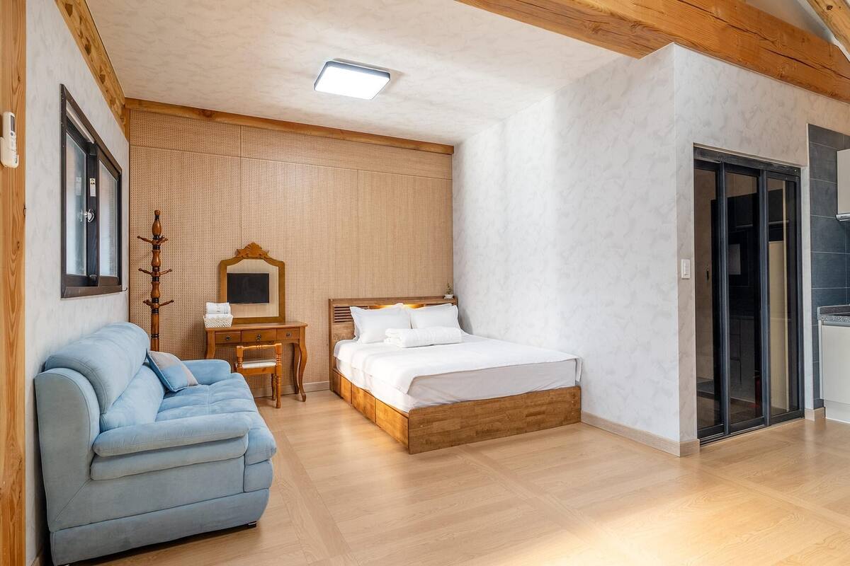 A bedroom with a wooden bed, a blue sofa, a small table, and a mirror.
