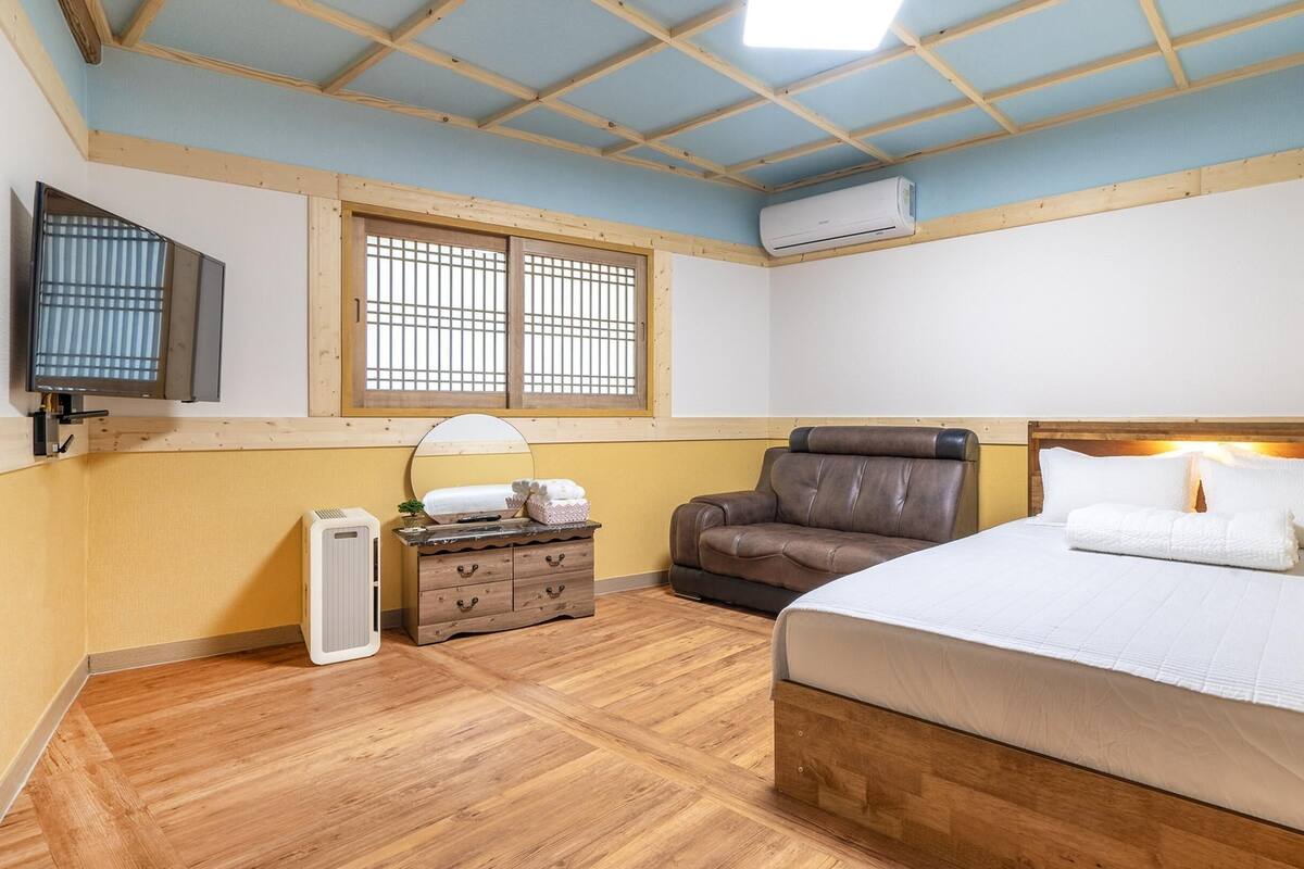 A bedroom with a bed, a chair, a dresser, a window, and an air conditioning unit.