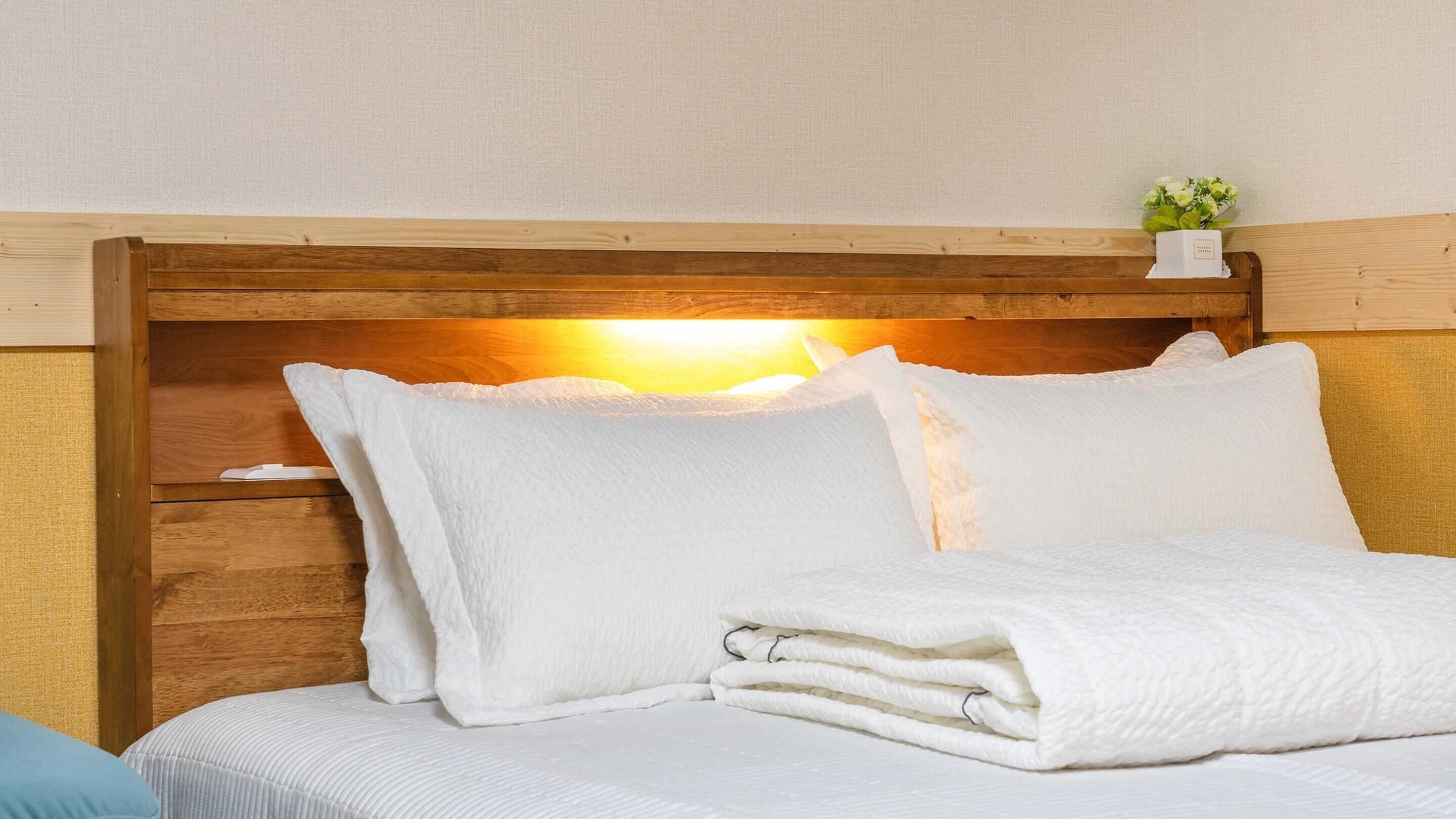Un lit bien fait, avec du linge de lit blanc, une tête de lit en bois et une petite plante posée sur la tête de lit.