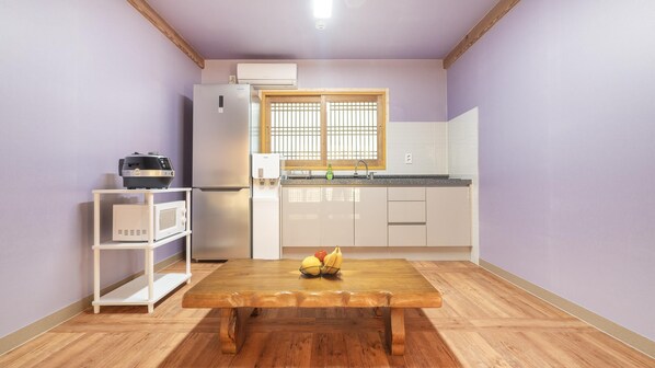 Une cuisine compacte équipée d’un réfrigérateur, d’un four à micro-ondes et d’une table en bois sur laquelle sont disposés des fruits.