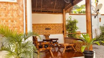 Relax in a serene outdoor seating area with a thatched roof, comfortable furniture, and lush greenery.